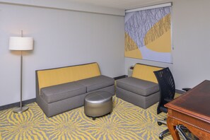 A hotel room with a sofa, ottoman, and a desk.