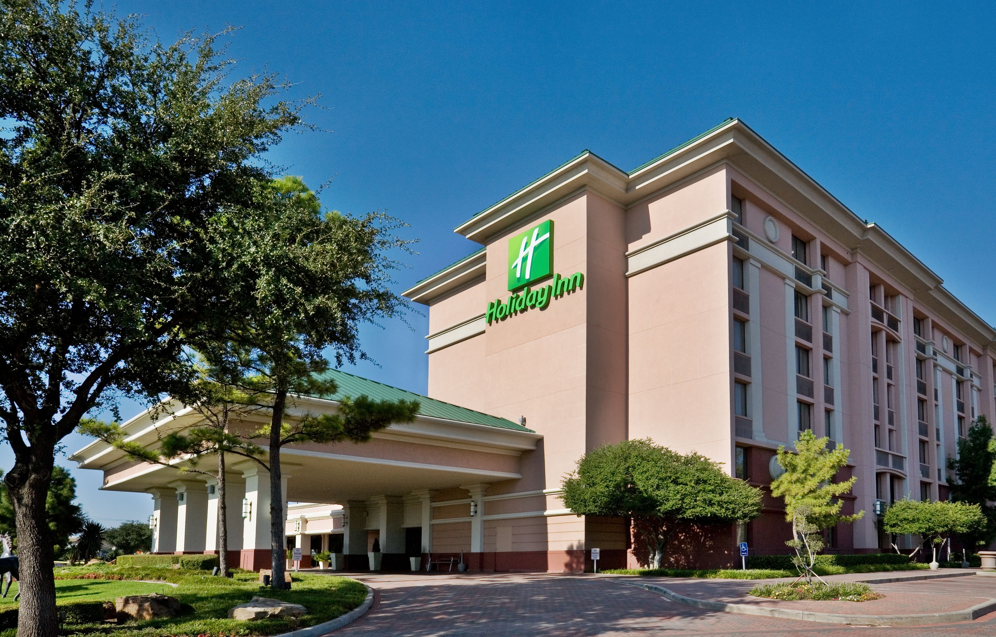 Holiday Inn -hotelli, jossa on suuri rakennus, katettu pysäköintialue ja hyvin hoidettu piha-alue.