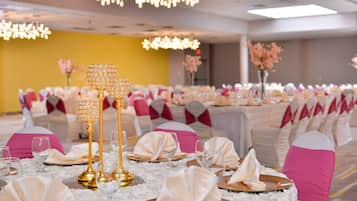 A banquet hall with round tables set for a formal event, featuring golden candelabras and white tablecloths.