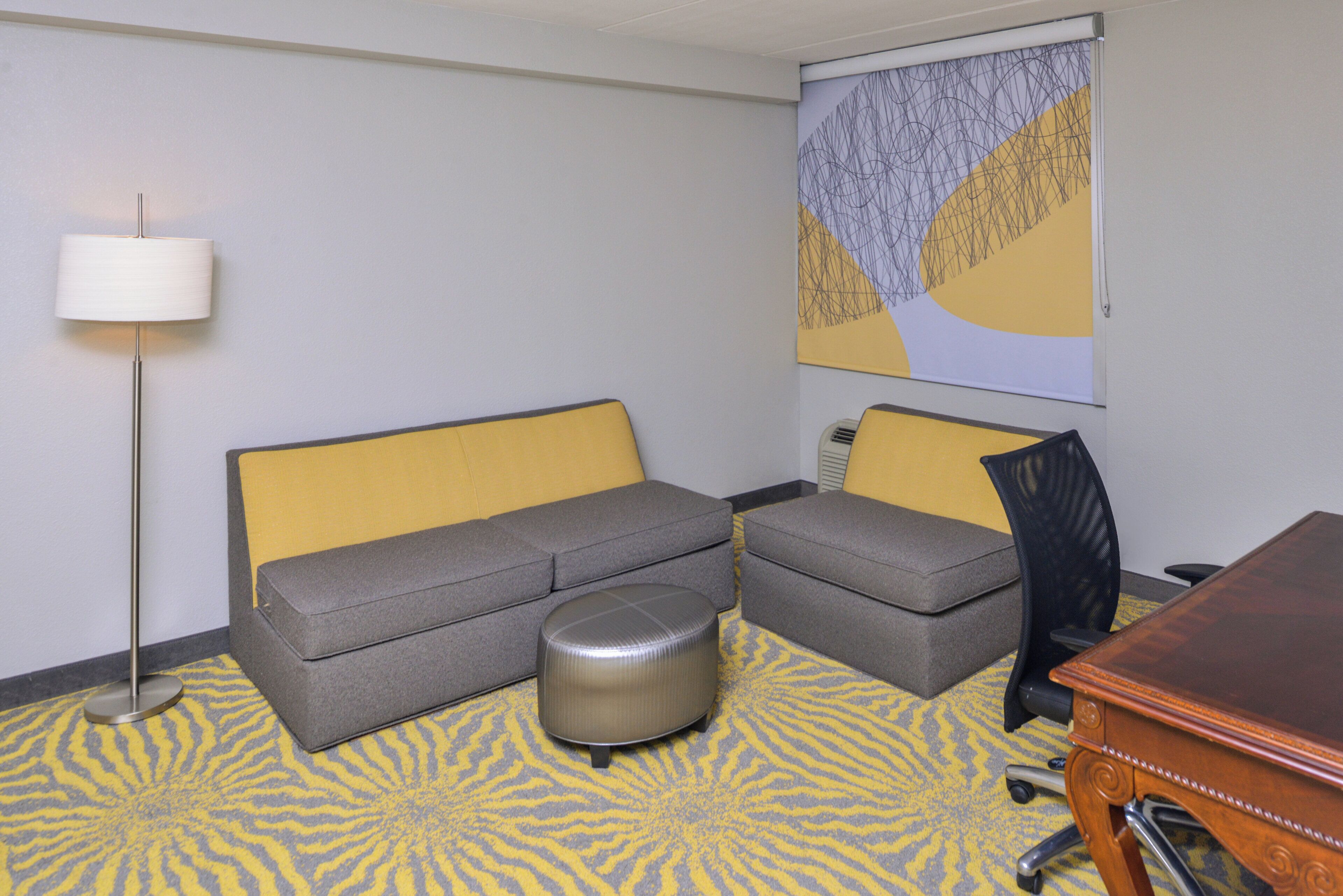 A hotel room with a sofa, ottoman, and a desk.