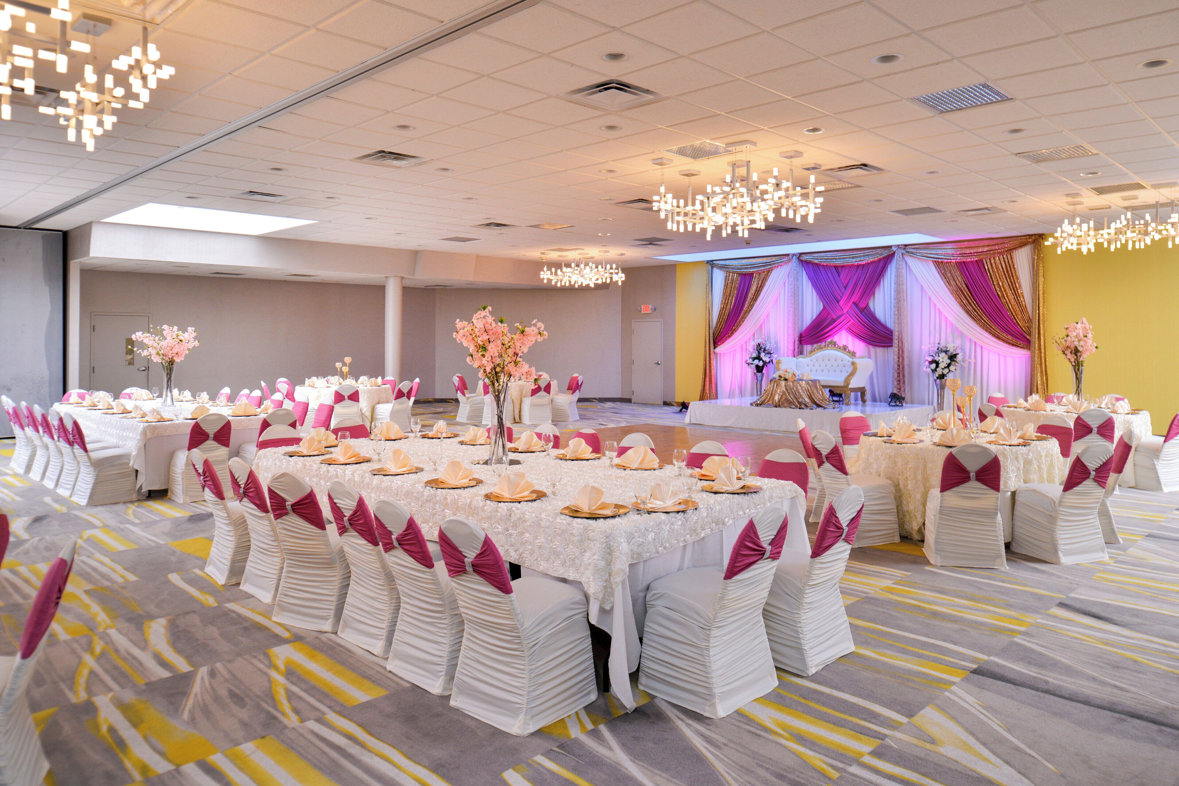 A banquet hall with round tables, chairs, and a stage with draped curtains.