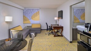 A hotel room with a glass dining table, a sofa with cushions, a desk with a lamp, a microwave, and a coffee maker. - Holiday Inn Dallas-Richardson by IHG (Richardson)