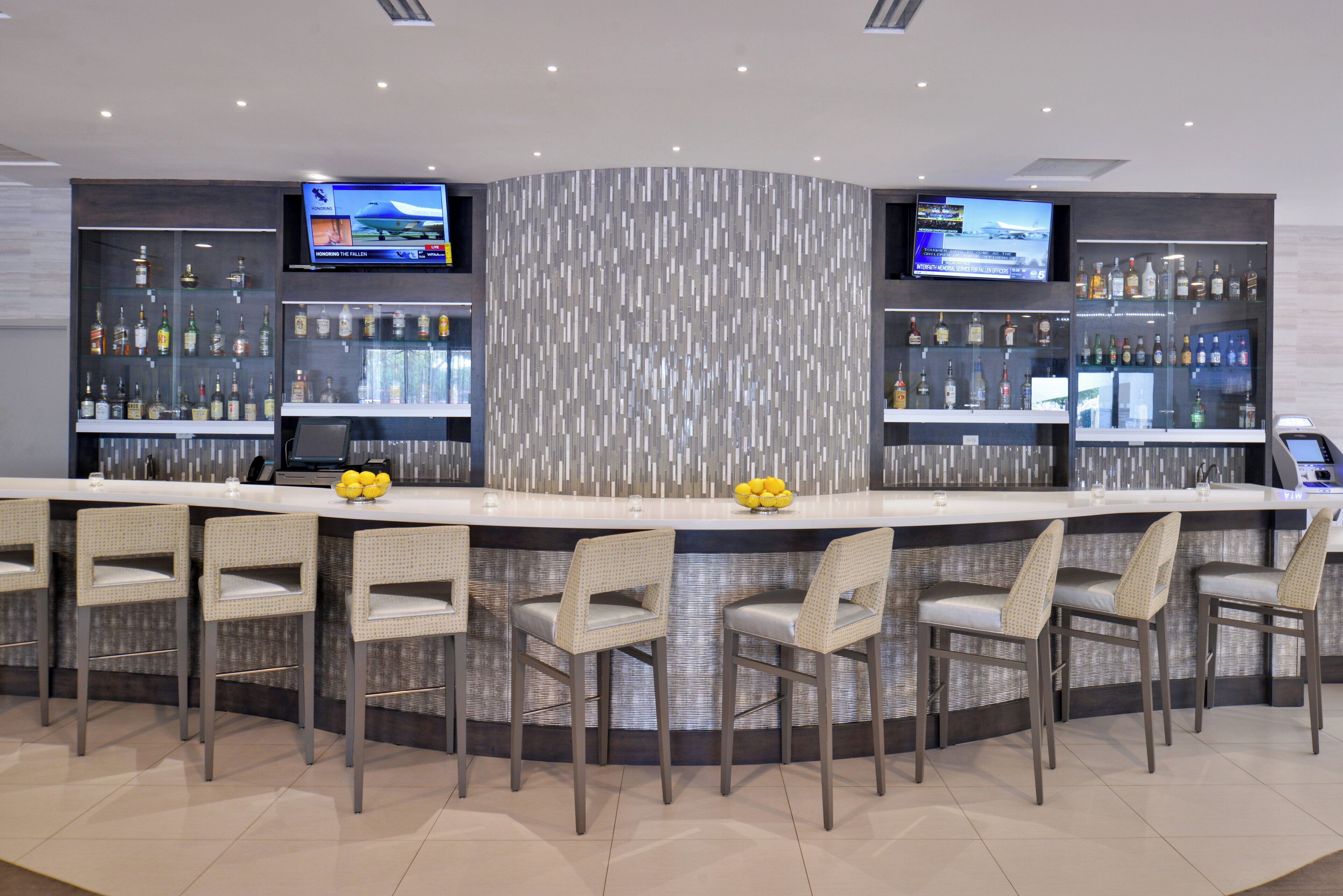 A bar area with a curved counter, multiple seating options, and two televisions mounted on the wall.