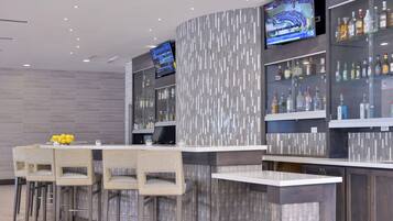 Zona de bar con diseño moderno, que incluye un televisor de pantalla plana, diversas botellas de licores y un conjunto de asientos con sillas y una mesa.