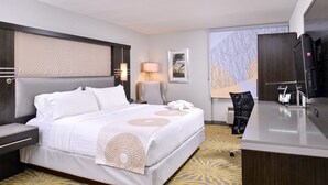 A hotel room with a large bed, a desk with a computer, a chair, a TV, and a window with a view of the city. - Holiday Inn Dallas-Richardson by IHG (Richardson)