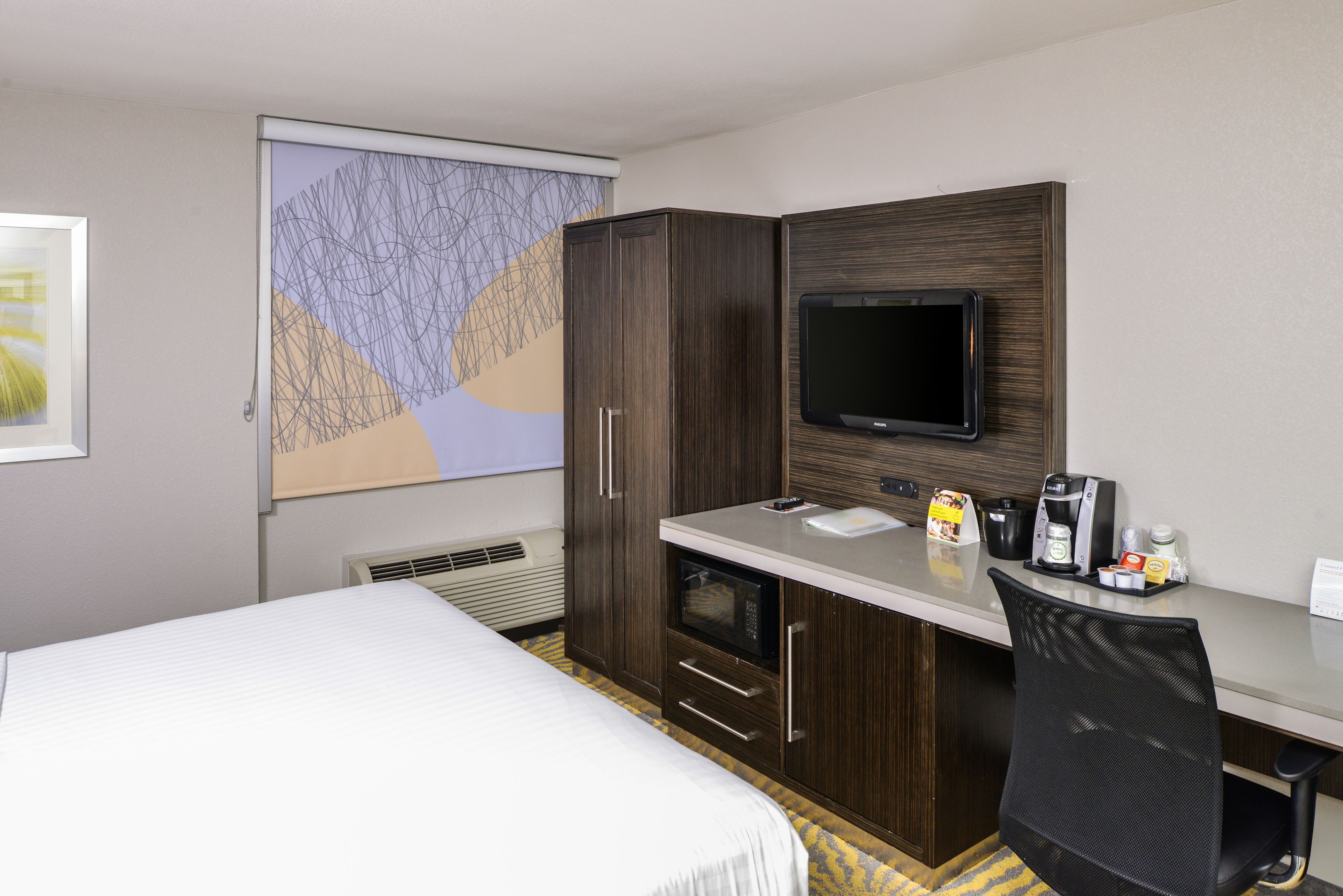 A hotel room with a bed, a desk with a flat-screen TV, a microwave, and a coffee maker.