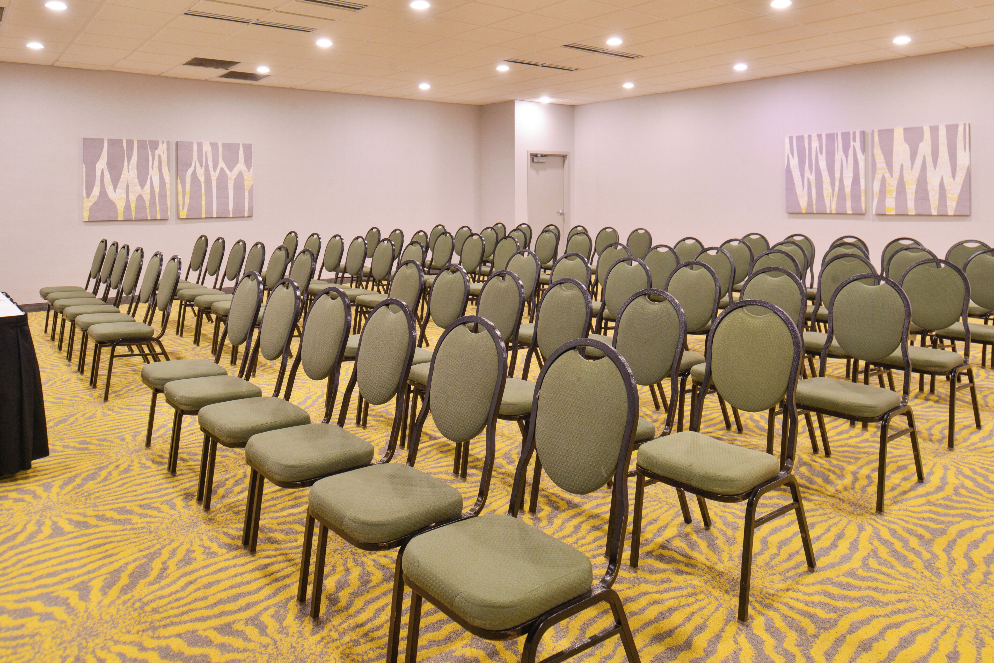 A conference room with rows of chairs, a carpeted floor, and abstract wall art.