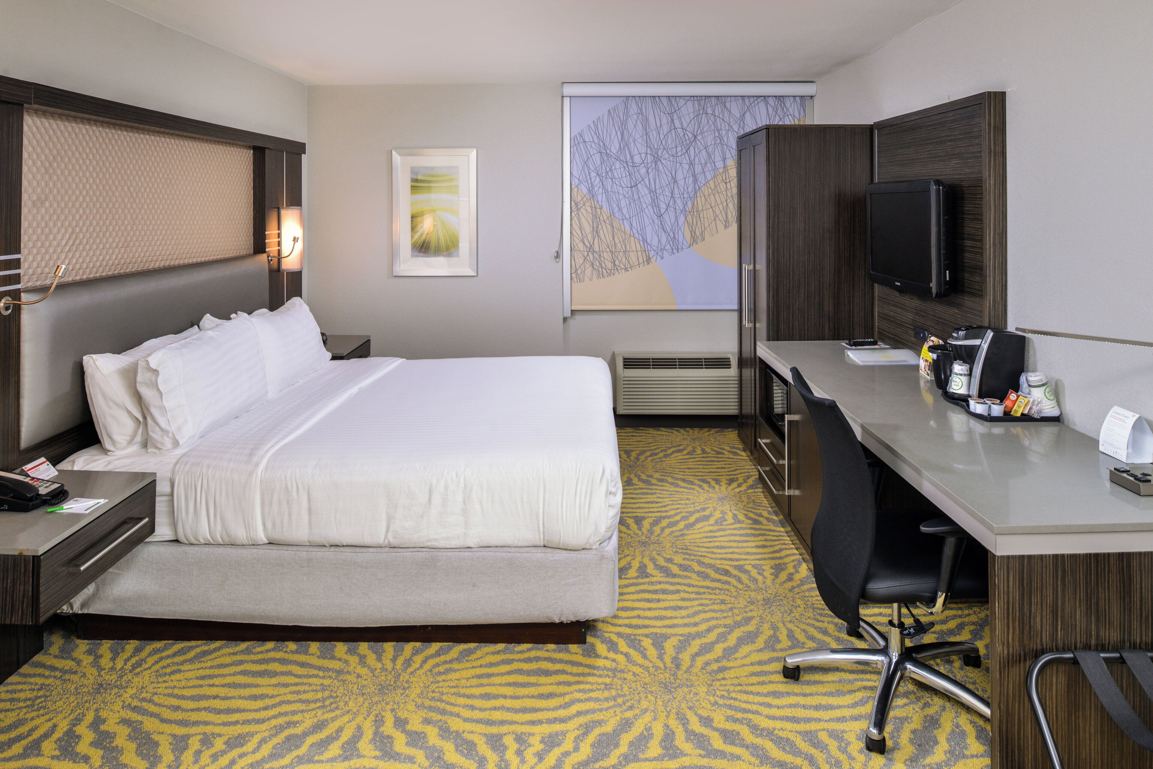 A hotel room with a bed, desk, chair, and a television.