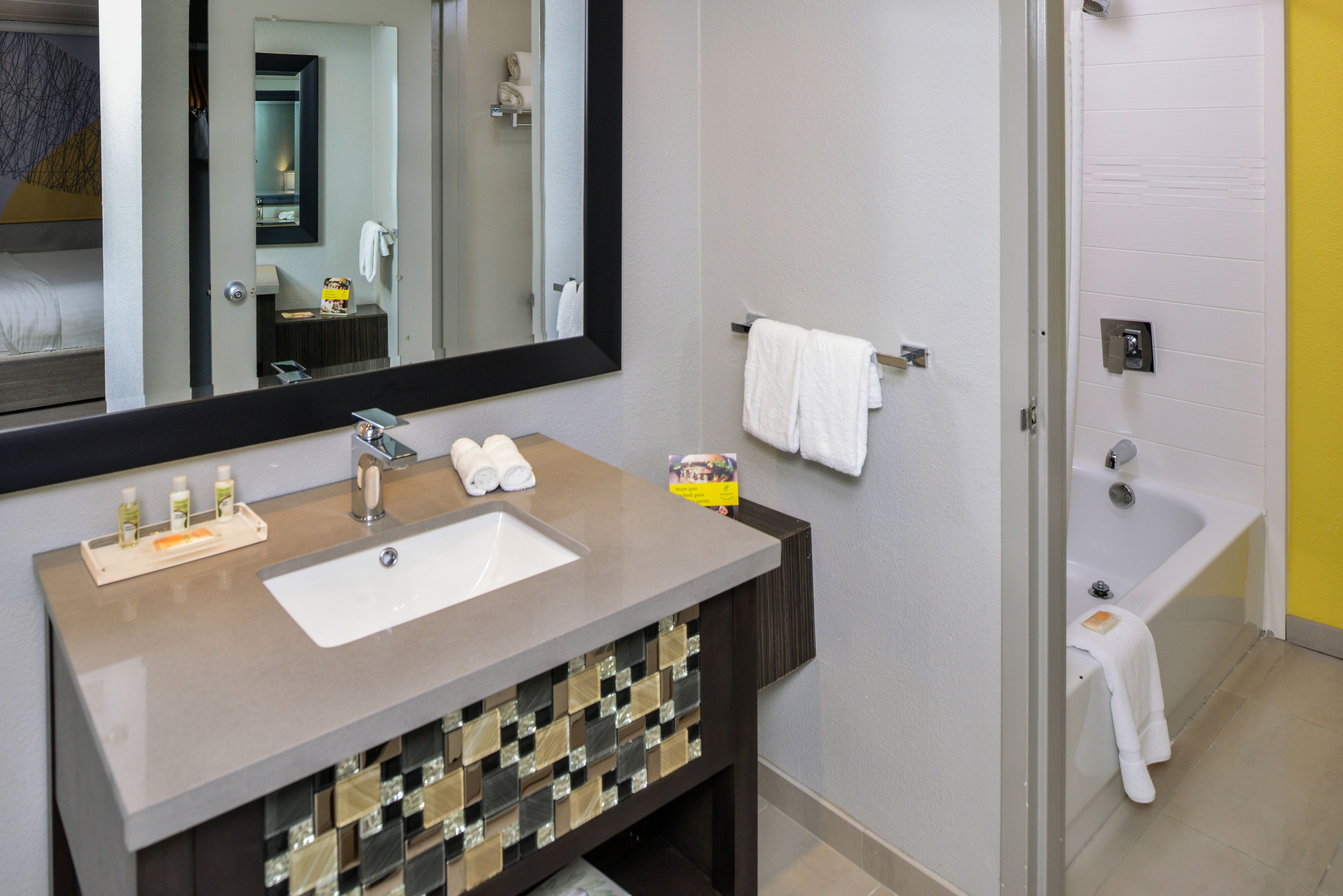 A bathroom with a sink, mirror, and bathtub.