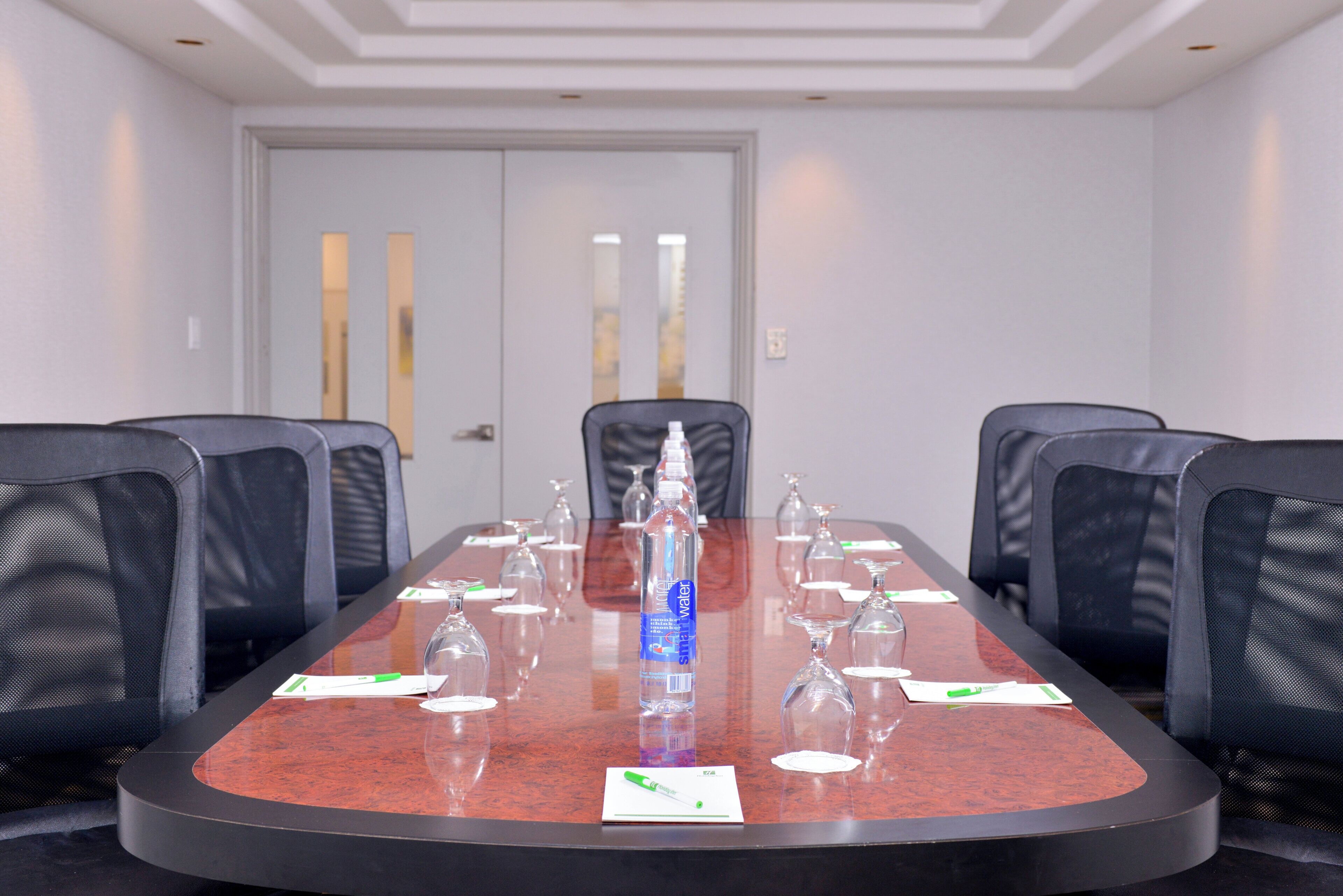 Un salón de conferencias con una mesa larga, seis sillas y un dispensador de agua.