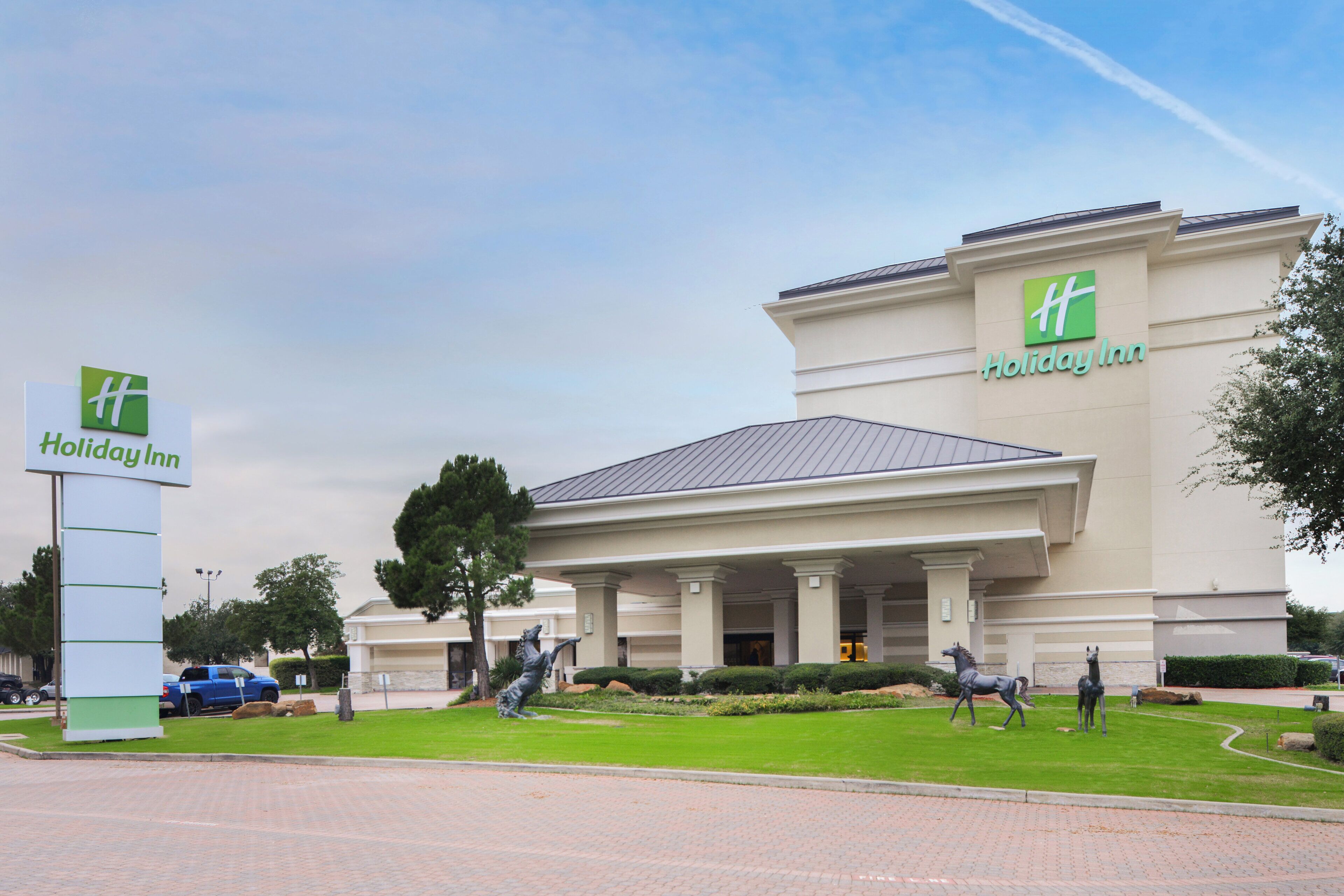 Un hotel Holiday Inn con un cartel grande, un acceso cubierto y una estatua de un caballo.
