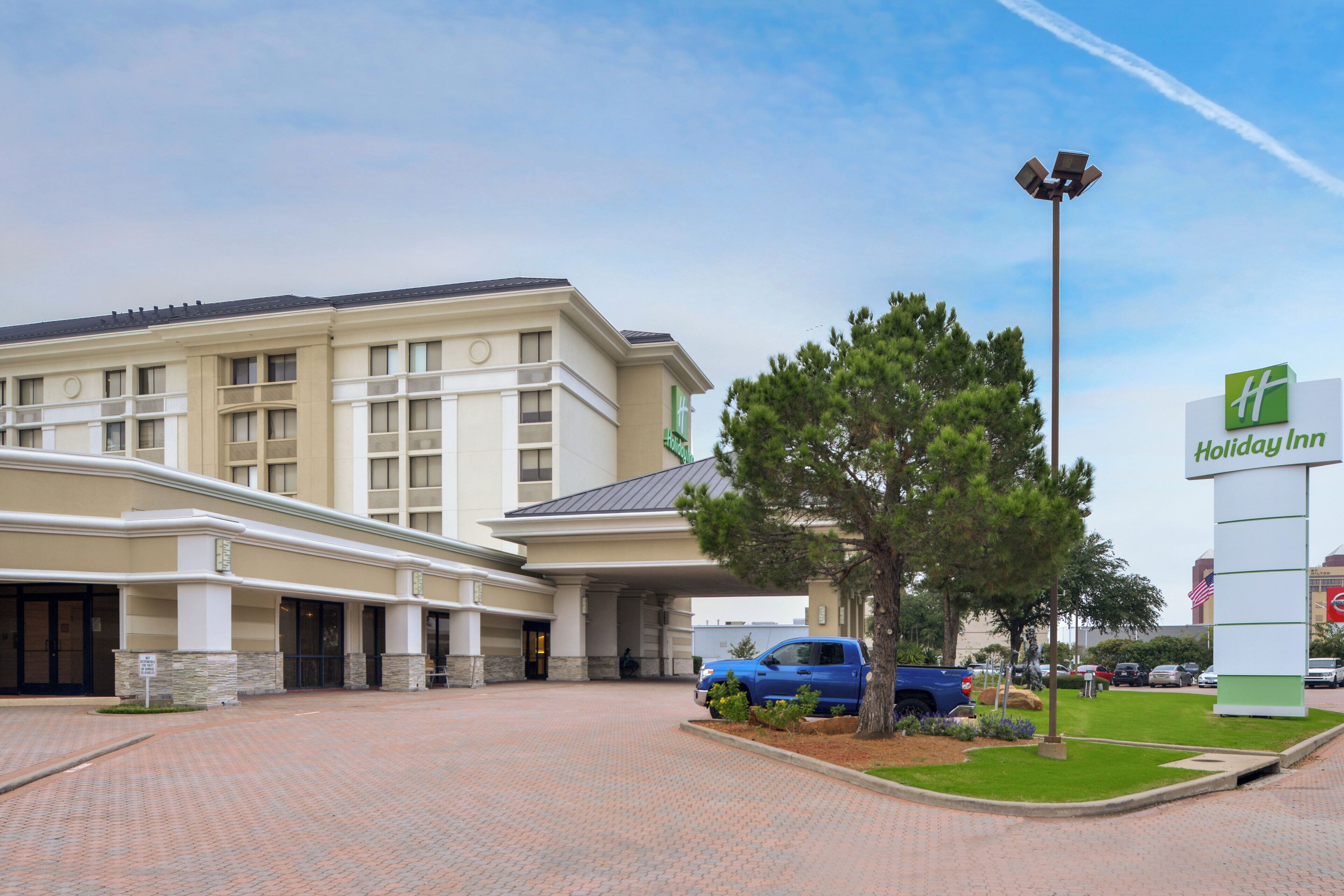 A Holiday Inn hotel with a brick entrance, a blue vehicle parked in front, and a signboard.
