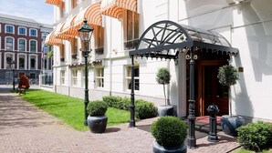 A hotel entrance with a covered entrance, a large potted plant, and a street lamp. - Carlton Ambassador Hotel (The Hague)
