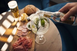 A glass of cocktail with ice, lime, and rosemary, a bottle of champagne, and various meats on a wooden board. - Carlton Ambassador Hotel (The Hague)