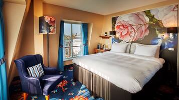 A hotel room with a large bed, a chair, a desk with a lamp, and a window with curtains.