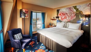 A hotel room with a large bed, a chair, a desk with a lamp, and a window with curtains.