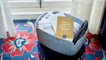 Een kamer met een raam, een bed met een grijze hoofdbord, een vloerkleed met blauw en rood patroon, en een kaartje op het bed.