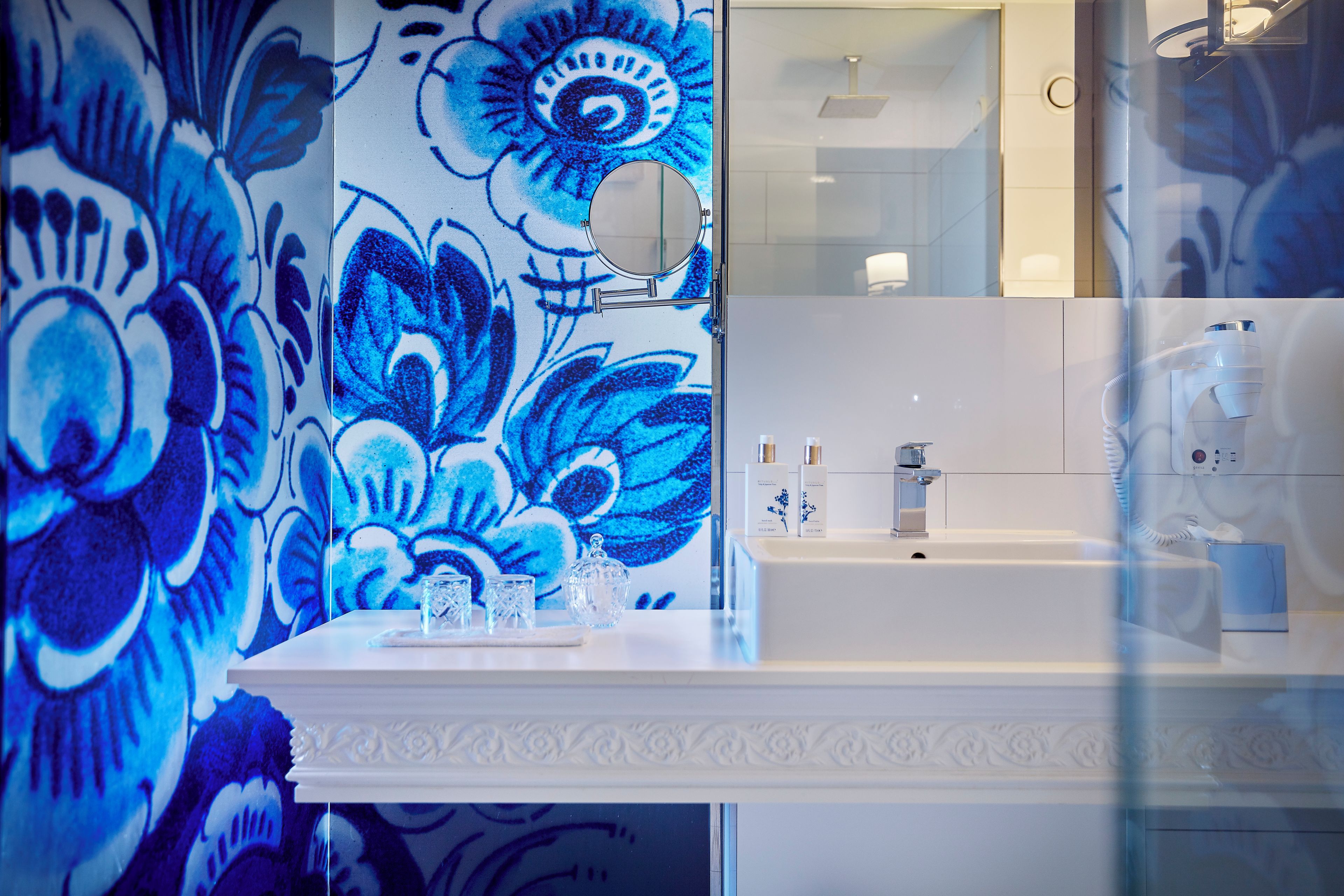 A bathroom with a floral wall design, a white sink, and a mirror.