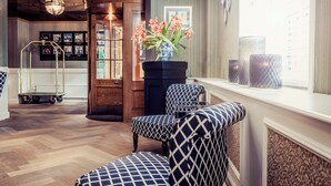 A hotel lobby with patterned chairs, a vase with flowers, and a view of the city through large windows. - Carlton Ambassador Hotel (The Hague)