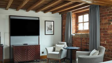 A room with a TV, two armchairs, a small table, a floor lamp, and a brick wall.