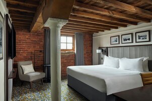 A hotel room with a brick wall, a large bed, a chair, and a window with curtains.