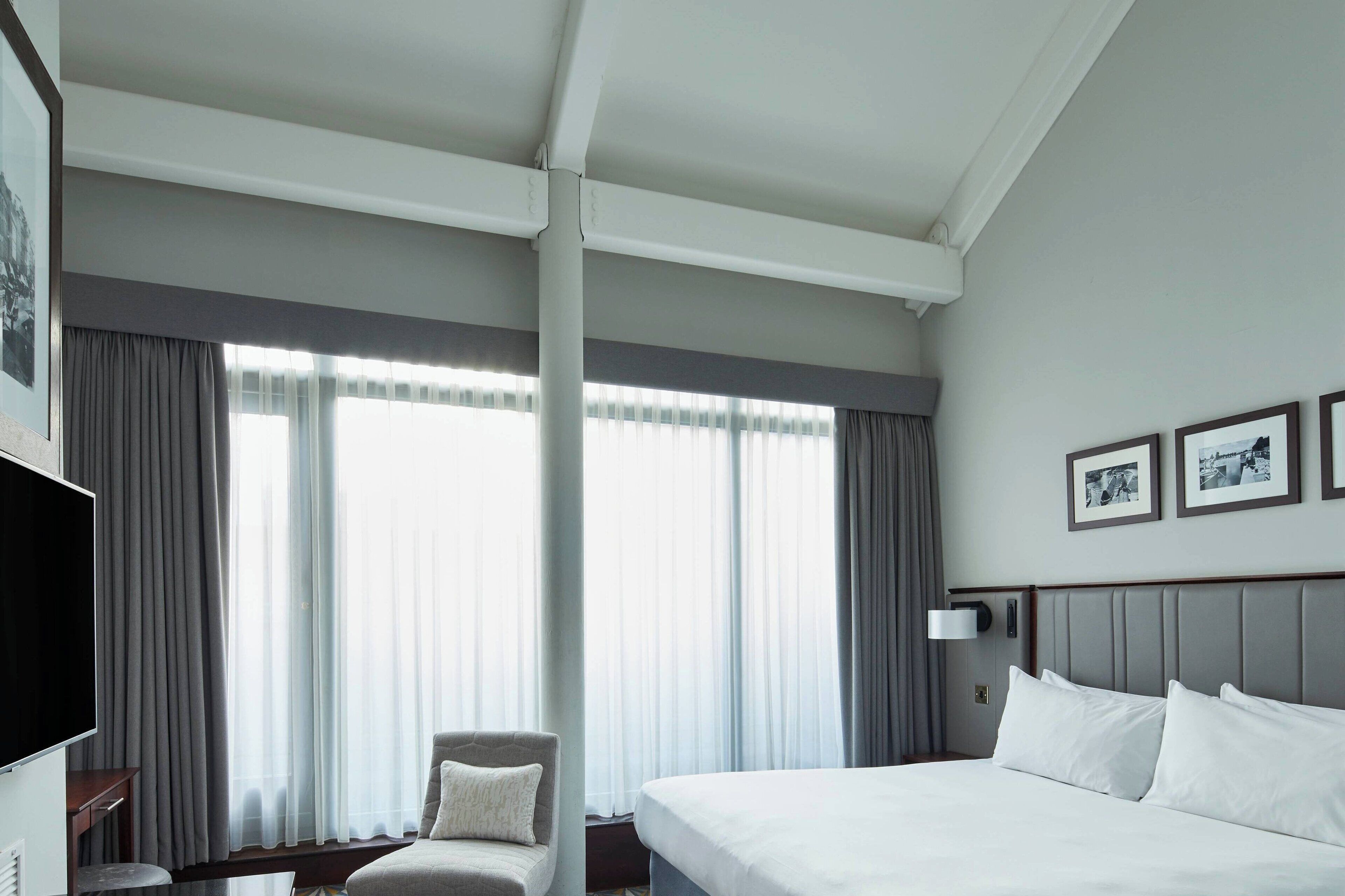 A hotel room with a large bed, a chair, a flat-screen TV, and a window with curtains.