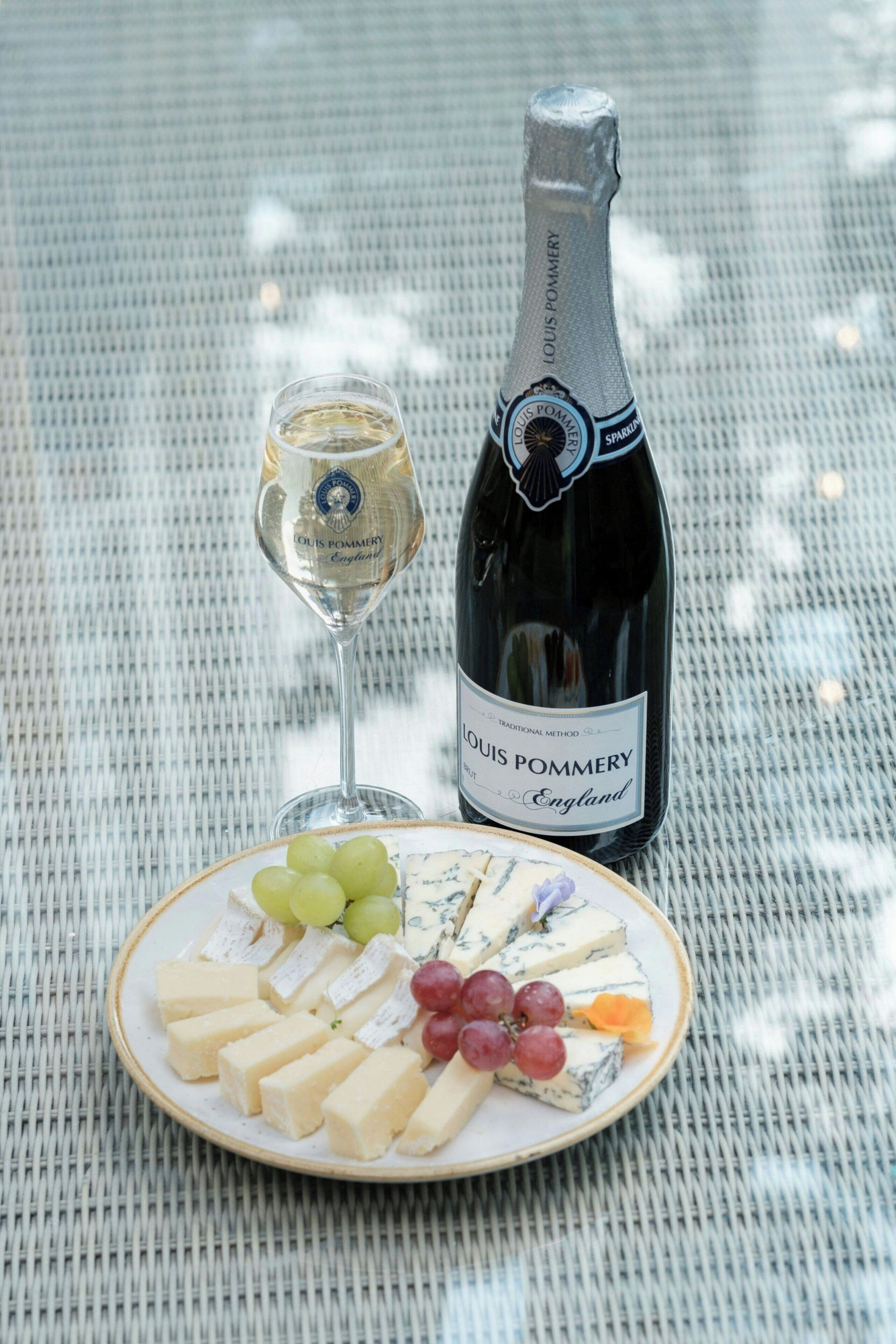 Eine Flasche Louis Pommery Champagner und ein Champagnerglas auf einem Tisch, zusammen mit einer Käseplatte und Trauben.