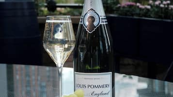 A bottle of Louis Pommery champagne, a glass of champagne, and a plate with cheese and grapes on a table with a city view in the background.
