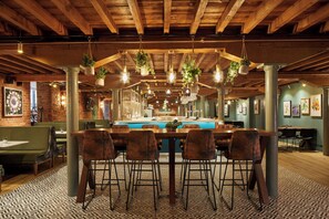 Un espace bar avec une table de billard, des tabourets de bar, des plantes suspendues et un mur en briques.