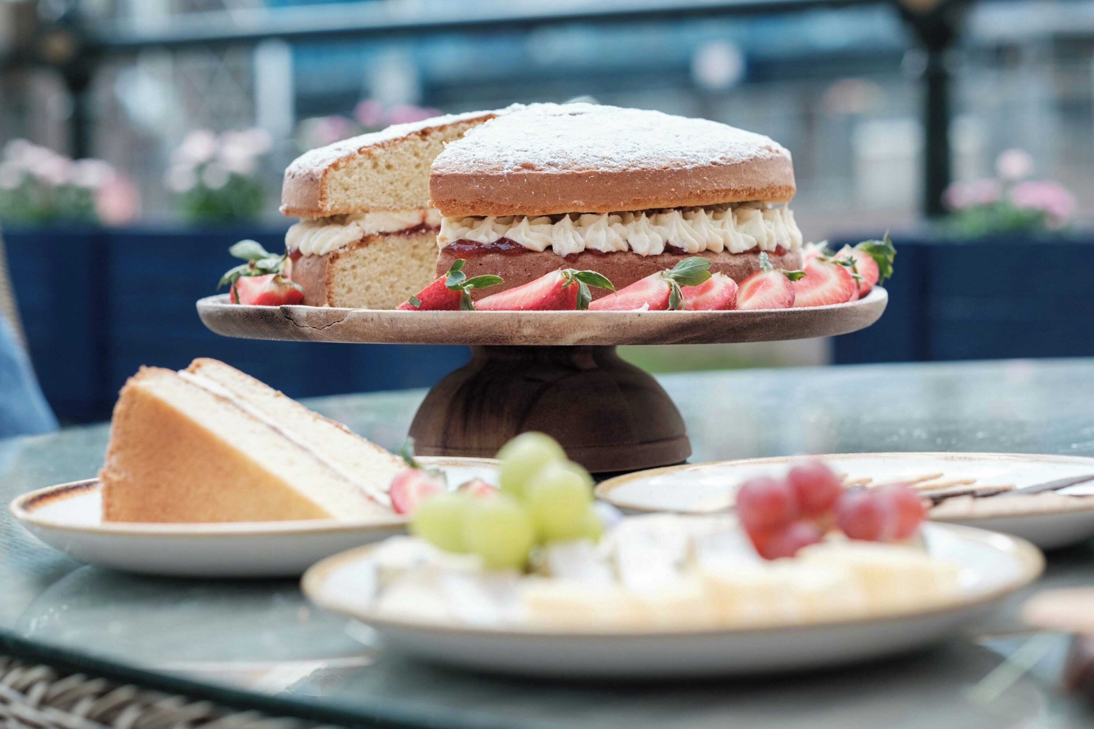 A layered cake with strawberries and whipped cream on a glass table.