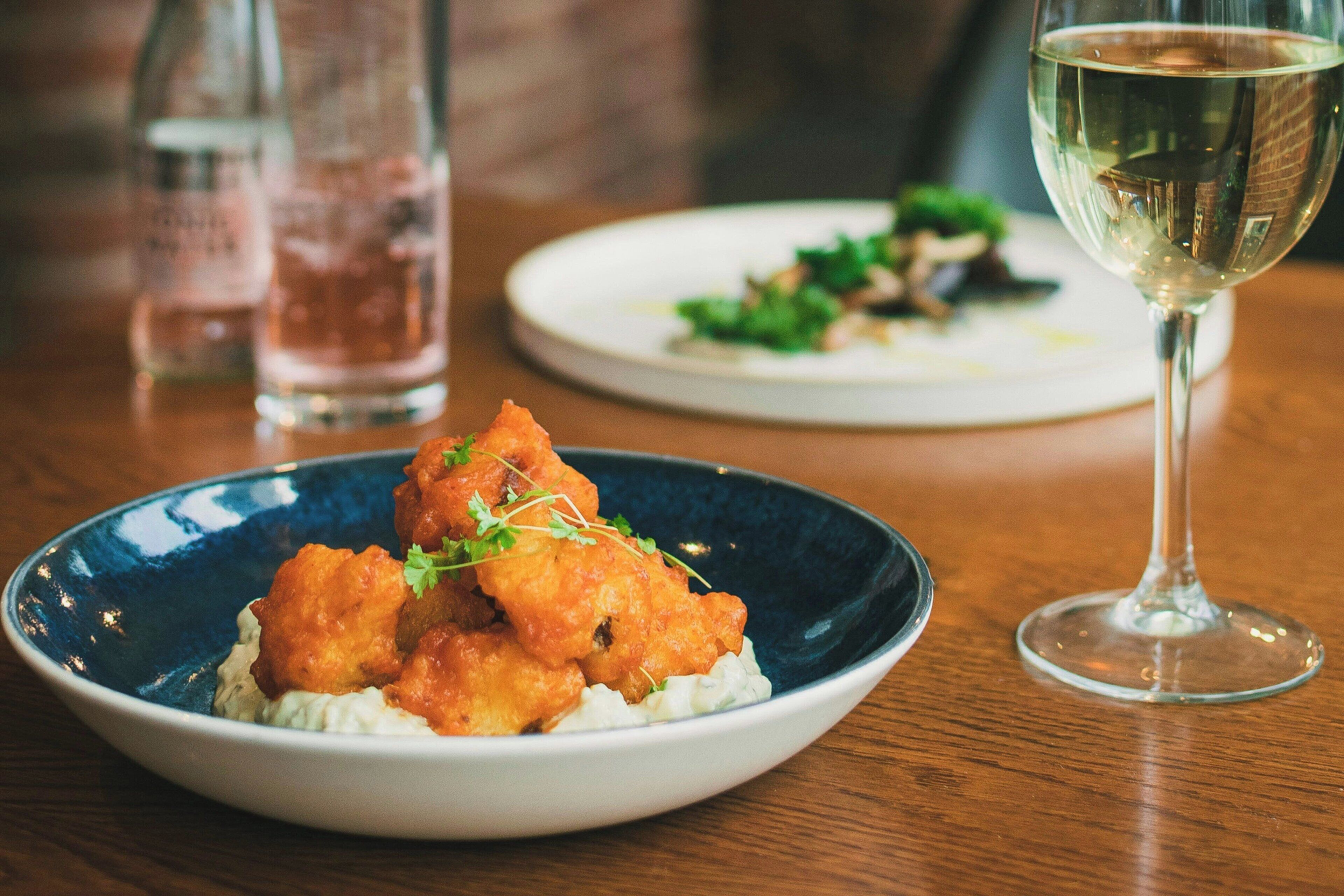 Ein Esstisch mit einem blauen Teller mit Essen und einem Glas Weißwein.