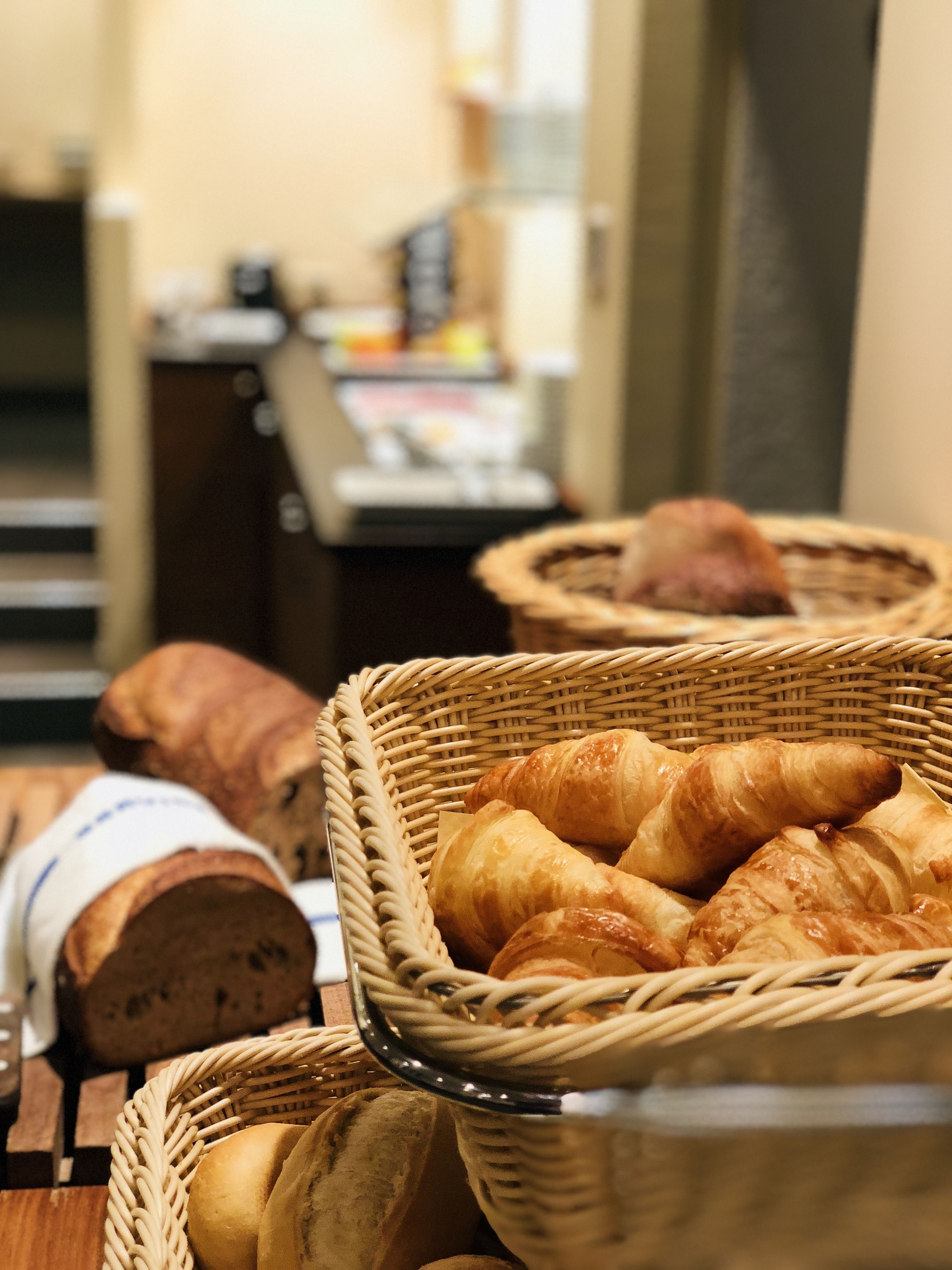 A variety of baked goods in wicker baskets, including croissants and baguettes, on a wooden surface.