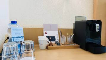 Un mostrador de recepción de hotel con dispensador de agua, una cafetera, un vaso de agua, una taza y una tarjeta.