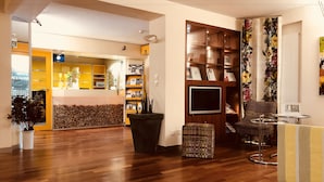 A hotel lobby with a wooden floor, a reception desk, a bookshelf with certificates, and a floral curtain. - Hotel Felmis (Horw)