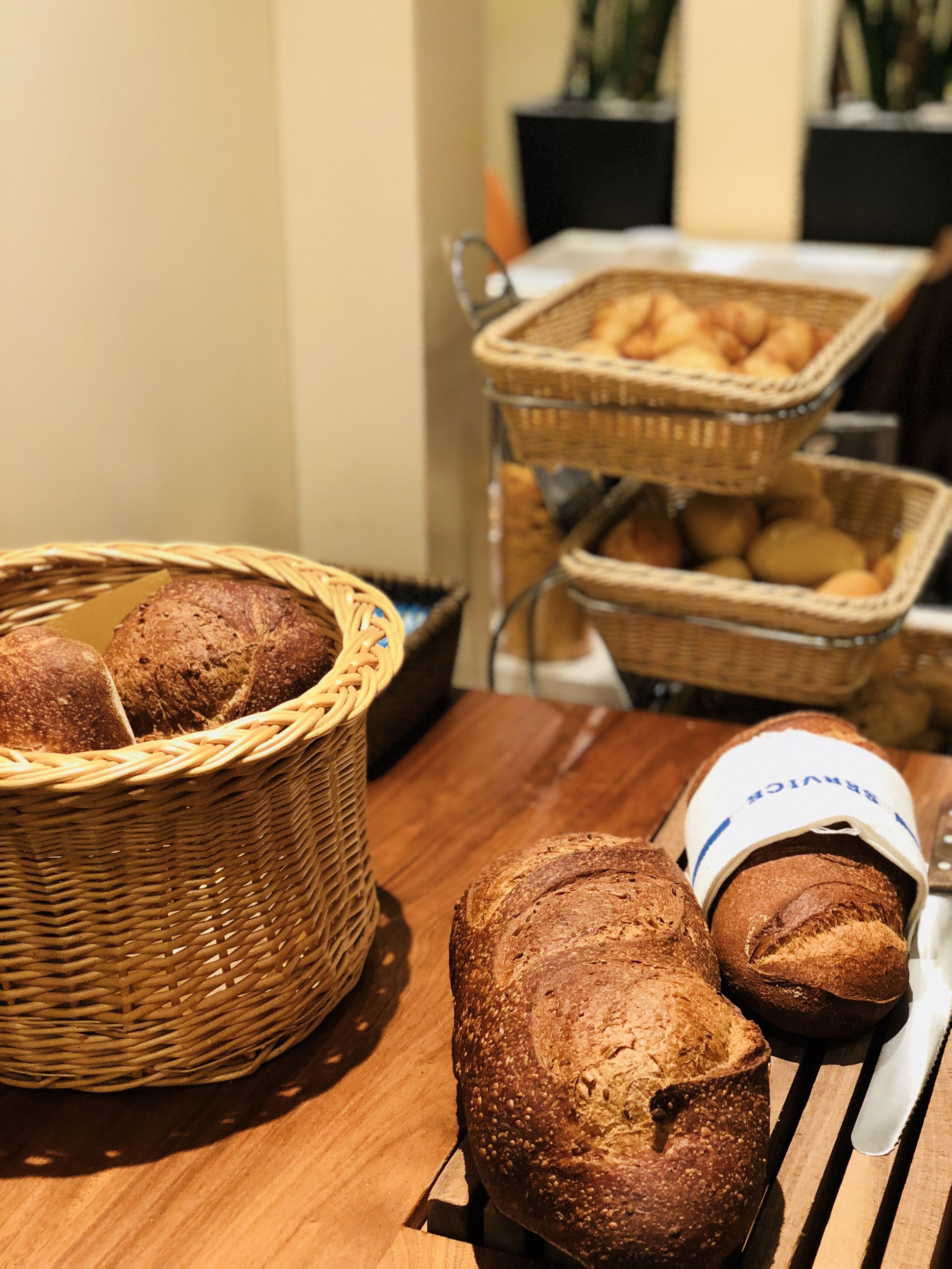 A wooden table with baskets of bread and a loaf of bread on a cutting board.