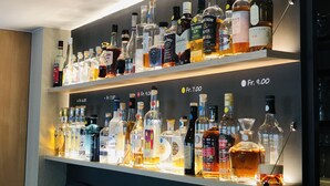 A bar with multiple shelves of liquor bottles, each labeled with prices. - Hotel Felmis (Horw)