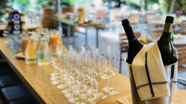 A long table with wine bottles and glasses, set outdoors with a view of trees and a building in the background. - Hotel Felmis (Horw)