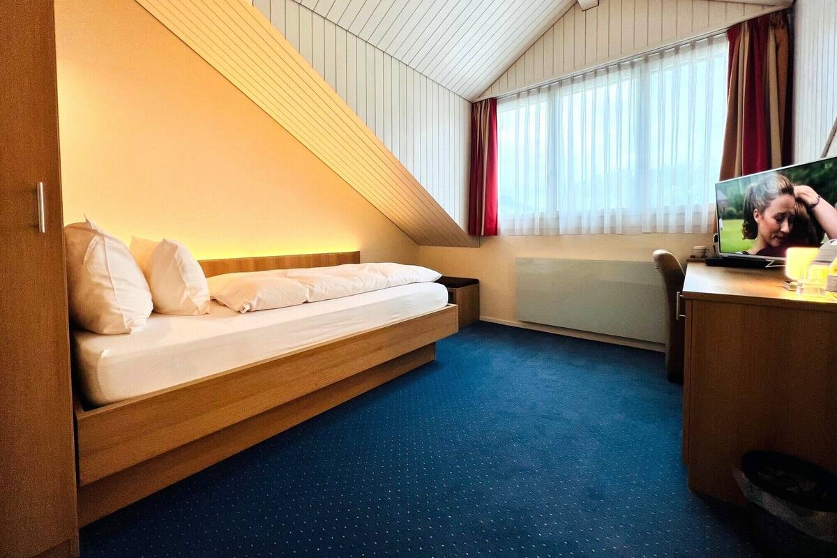 A compact hotel room with a bed, a desk, and a television.