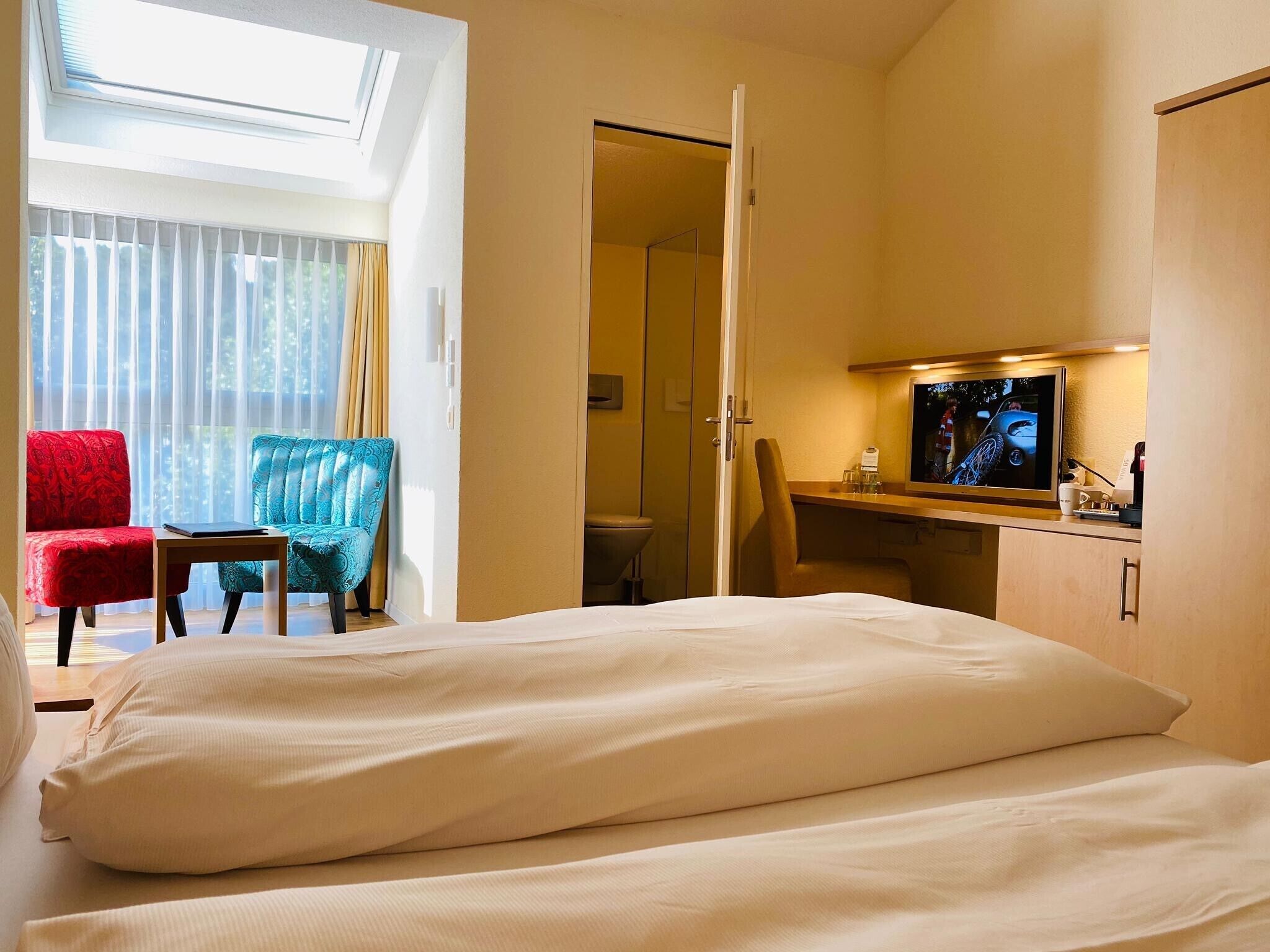 A hotel room with a bed, a desk, a TV, and two chairs.