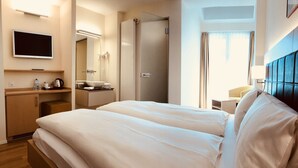 A hotel room with a large bed, a TV mounted on the wall, a bathroom with a mirror, and a window with curtains. - Hotel Felmis (Horw)