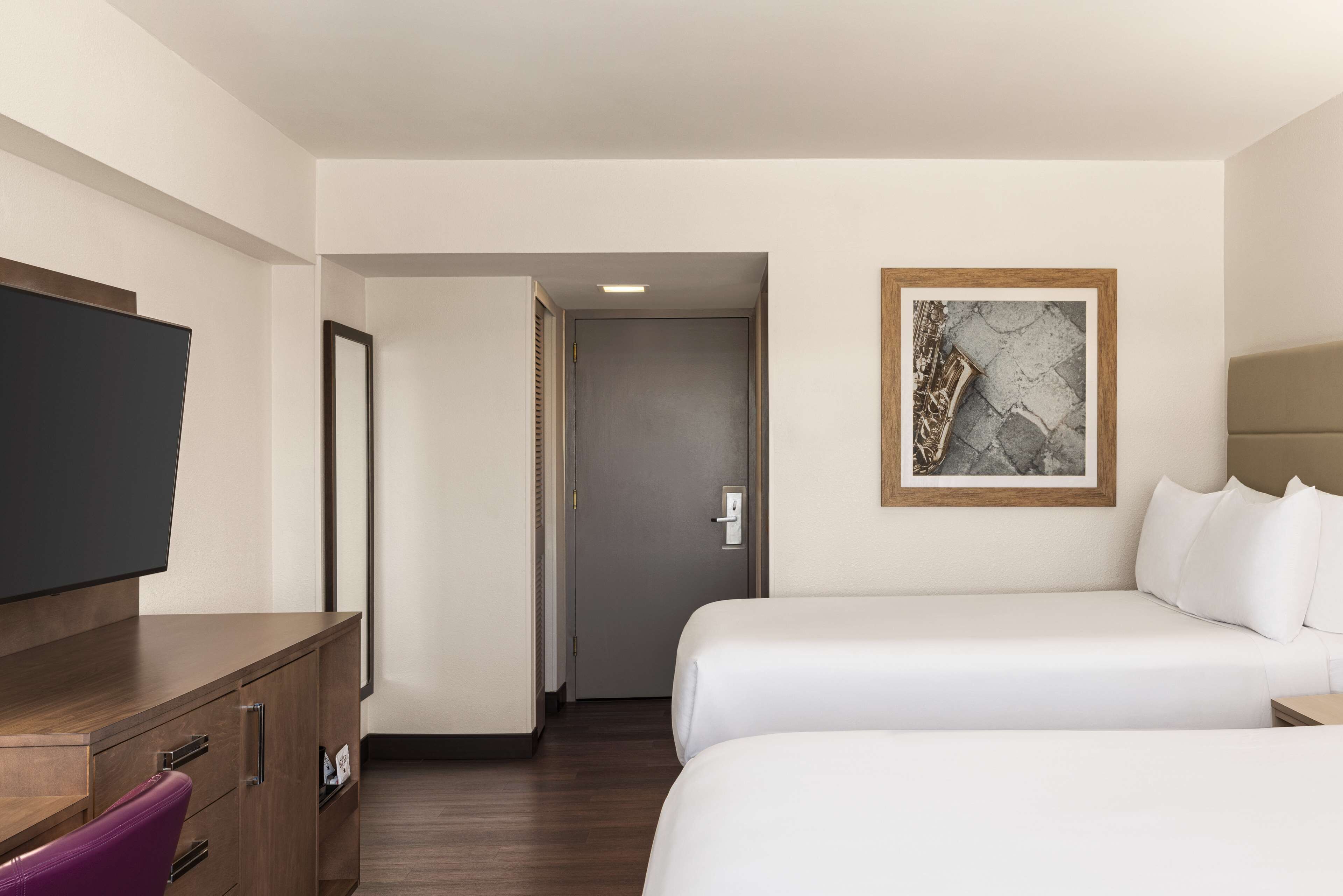A hotel room with a bed, a TV, a desk, and a door leading to another room.