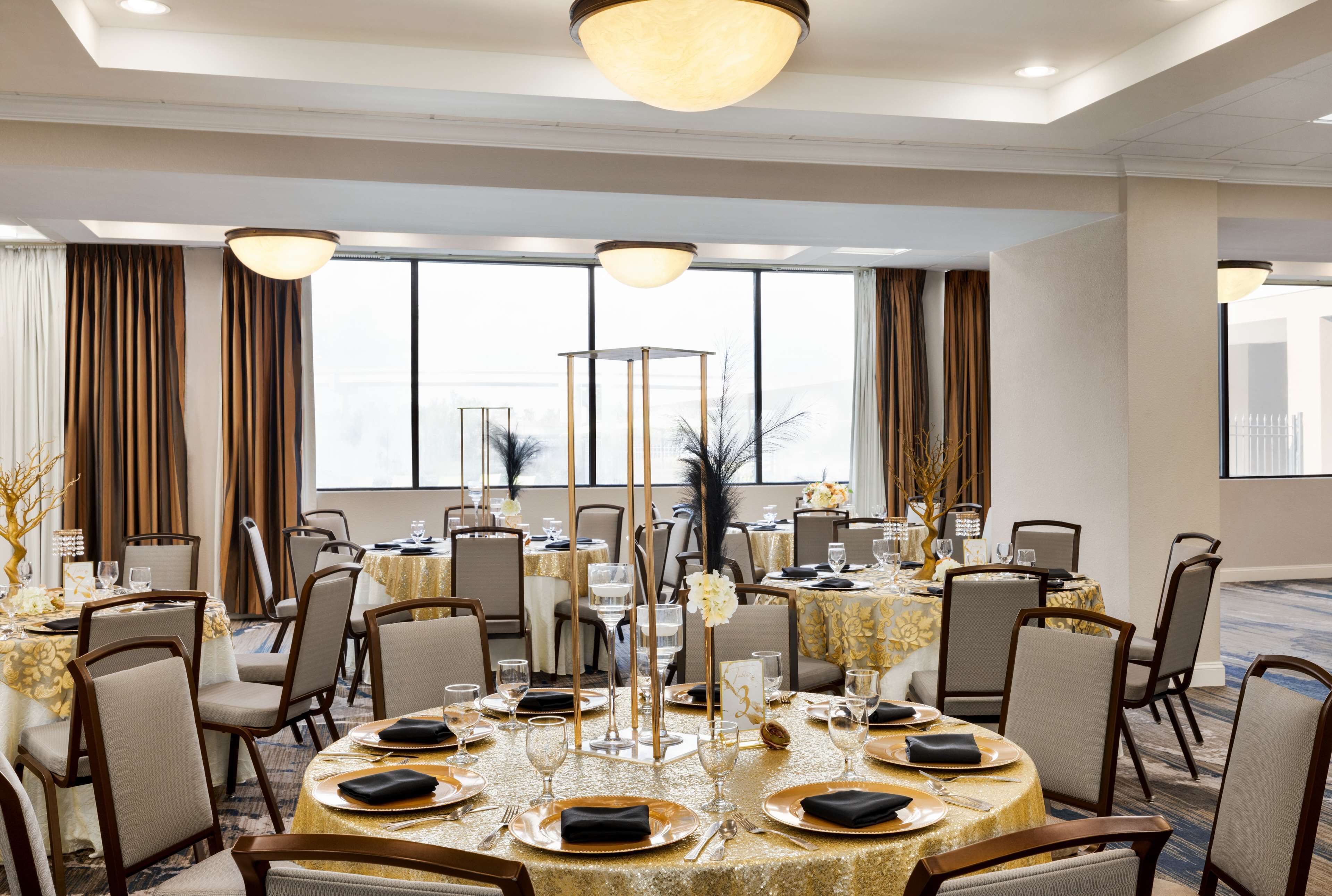 Un salón de banquetes con mesas redondas dispuestas para cenar, ventanas amplias y un techo alto con iluminación empotrada.