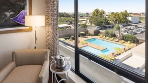 Habitación de hotel con vista a una piscina, una silla, una lámpara y una pequeña mesa con una jarras y vasos.