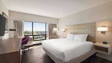 A hotel room with a large bed, a desk, a chair, and a TV.