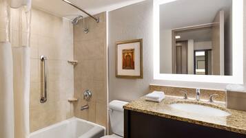 A modern bathroom with a walk-in shower, a bathtub, a sink with a granite countertop, and a large mirror.