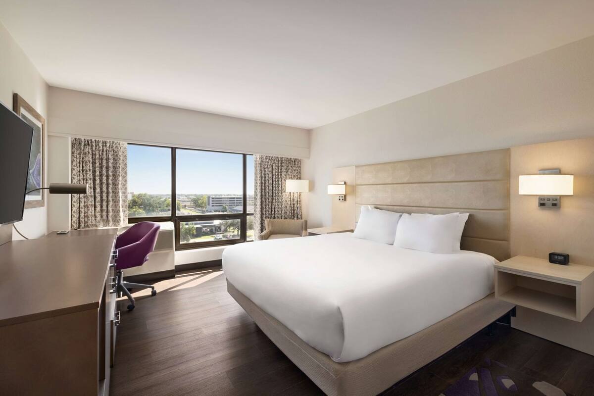 Habitación de hotel con una cama grande, un escritorio, una silla, un televisor y una ventana con vistas.