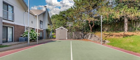 An outdoor basketball court with a hoop, surrounded by a residential area with houses and trees.