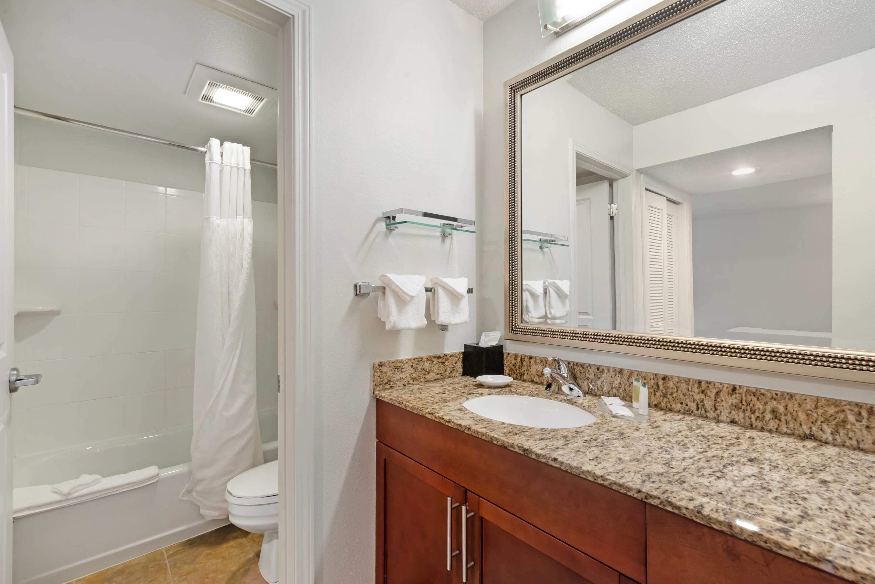 A bathroom with a shower, toilet, sink, and mirror.
