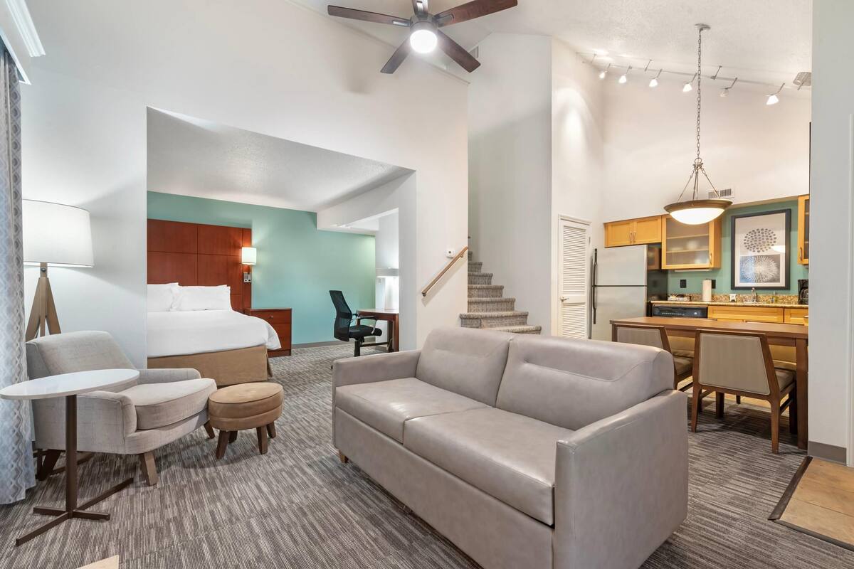 A hotel room with a bed, a sofa, a desk, and a kitchenette.