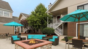 A patio area with a stone fire pit, outdoor seating, and umbrellas. - MainStay Suites St. Louis - Galleria (Richmond Heights)